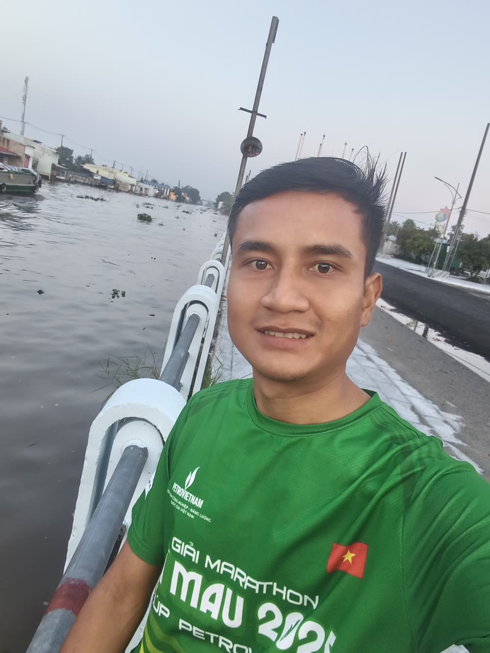 Minh mặc áo chạy xanh, chụp ảnh bên bờ sông