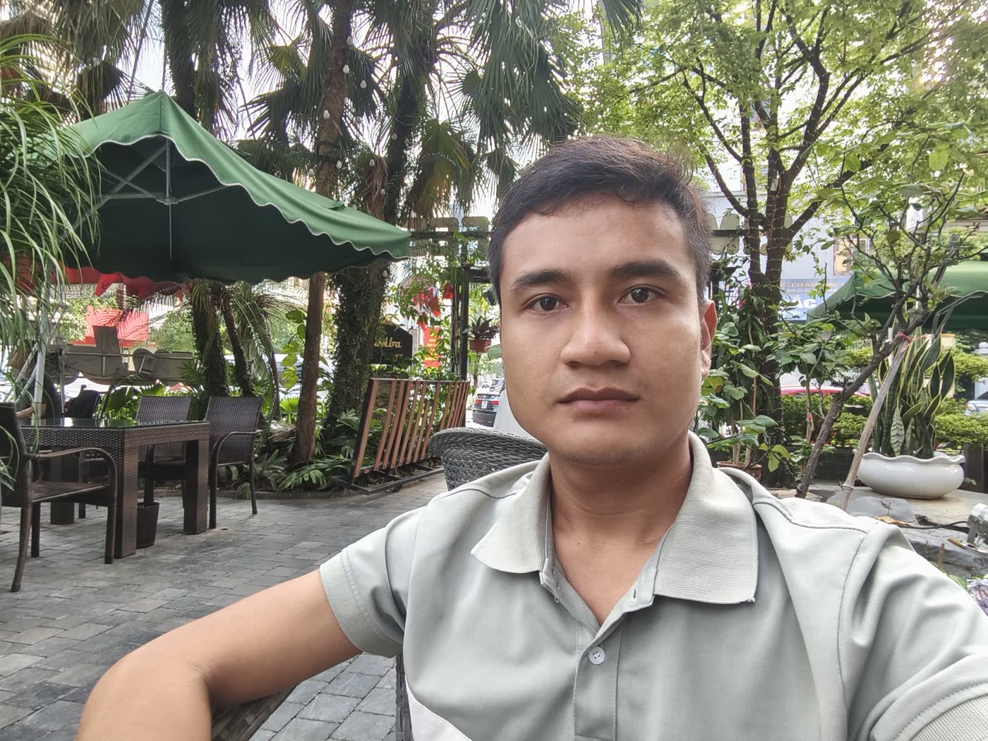 Minh mặc áo polo xám ngồi ở quán cà phê sân vườn